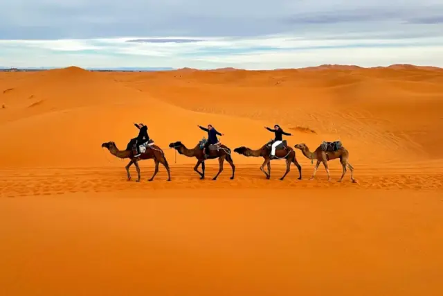Grupo de viajeros en dromedario cruzando las dunas de Erg Chebbi en Merzouga al atardecer